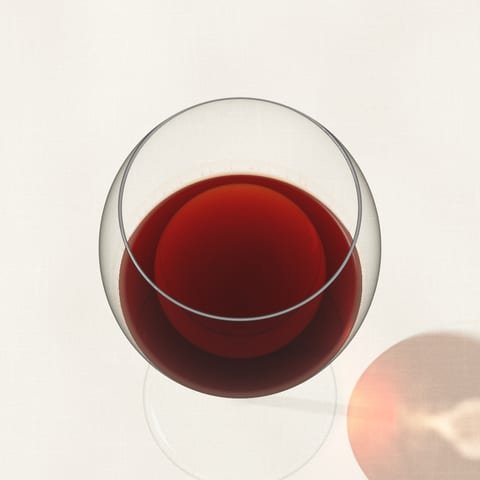 A glass of old red wine, brick at the rim, seen from above on linen