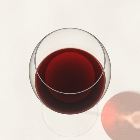A glass of garnet red wine with a brick edge, seen from above on linen