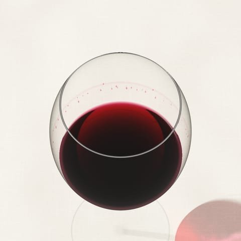 Close view of the inside wall of a wine glass, tears running down towards red wine